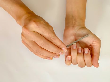 Woman's girl's hand filing nails with metal nail file on a white background. Self manicure at home