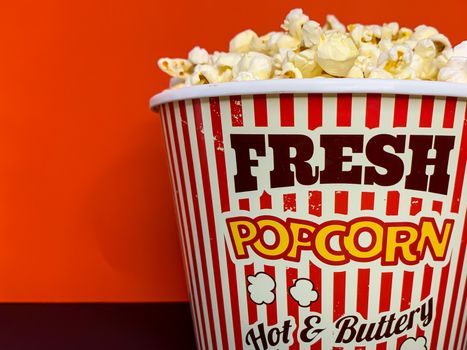Close up delicious fresh buttery popcorn in a stripped red and white bowl on red background with empty space for text