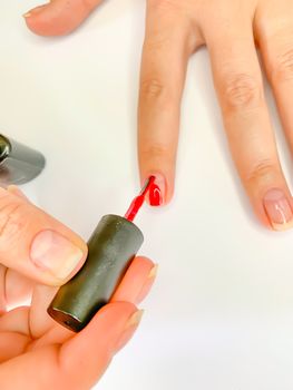 Close up female woman painting her nails with nail polish in red color on a white background. Self manicure at home