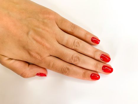 Close up female woman hand with red nails on a white background. Self manicure at home