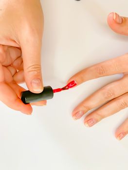 Close up female woman painting her nails with nail polish in red color on a white background. Self manicure at home