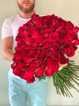 Bearded man in white t shirt holding in hands rich gift bouquet of 101 red rose. Front view