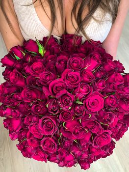 A young girl holding in hands a huge bouquet of 101 wonderful purple pink roses. Top view