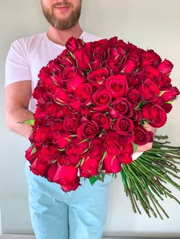 Bearded man in white t shirt holding in hands rich gift bouquet of 101 red rose. Front view