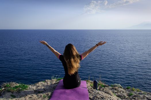 Beautiful young happy lonely girl sitting on rock and watching blue Mediterranean sea and relaxing