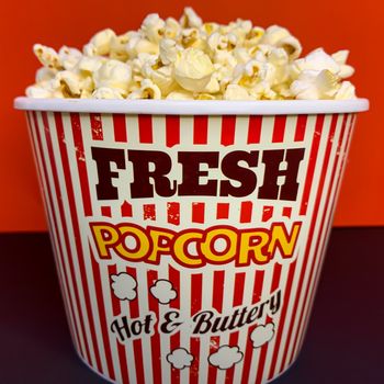 Close up delicious fresh buttery popcorn in a stripped red and white bowl on red background