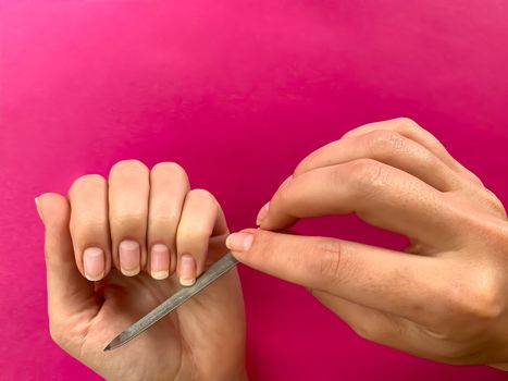 Woman's girl's hand filing nails with metal nail file on a pink background. Self manicure at home