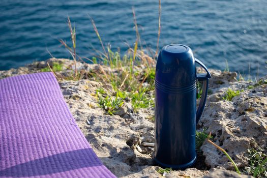 Blue thermos with tea picnic by the seaside on sunny day