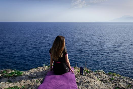 Beautiful young happy lonely girl sitting on rock and watching blue Mediterranean sea and relaxing