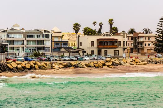 Sea waves, coastline cars and buildings on the street of Swakopmund German colonial town, Namibia