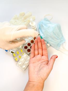 Hand of female in medical glove that applying alcohol spray or anti bacteria spray to prevent spread of germs, bacteria and virus on white background with medical tools and pills. Personal hygiene