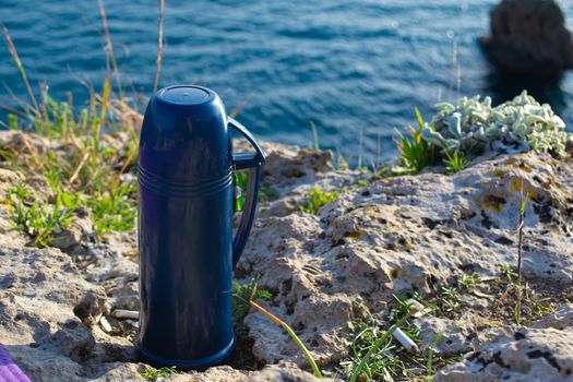 Blue thermos with tea picnic by the seaside on sunny day