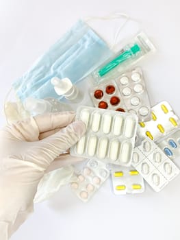 Tablets pills in hand in glove of a woman on white background with many pills and medicines. Vertical image