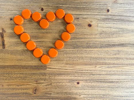 An orange love heart made from beer bottle tops lids on a rustic wooden table. Beer drinkers Valentine's day concept top view horizontal image with empty space for text