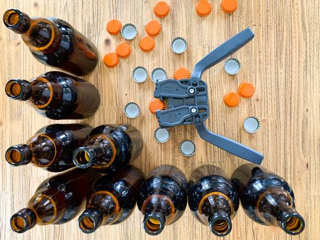 Beer brewing at home, plastic capper to put metal caps on bottles, brown glass beer bottles and orange crown caps on wooden background, horizontal image