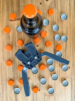 Beer brewing at home, plastic capper to put metal caps on bottles, brown glass beer bottle and orange crown caps on wooden background. Vertical image