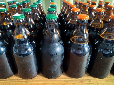 A lot of home brewery self made beer. Many brown glass craft beer bottles with green and orange corks, close up front view on a wooden table horizontal image.