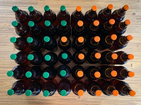 A lot of home brewery self made beer. Many brown glass craft beer bottles with green and orange corks, flat top view on a wooden texture horizontal image.