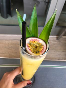 Delicious refreshing yellow exotic cocktail with passion fruit in girl's hand