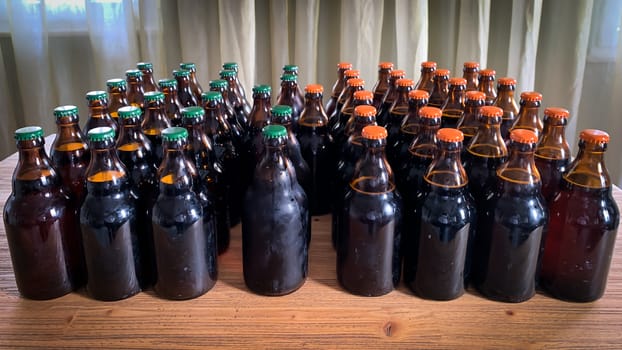A lot of home brewery self made beer. Many brown glass craft beer bottles with green and orange corks, front view on a wooden table horizontal image.