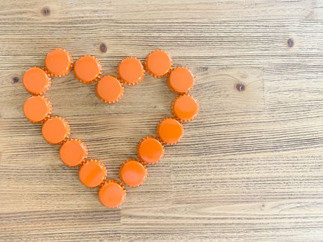 An orange love heart made from beer bottle tops lids on a rustic wooden table. Beer drinkers Valentine's day concept top view horizontal image with empty space for text