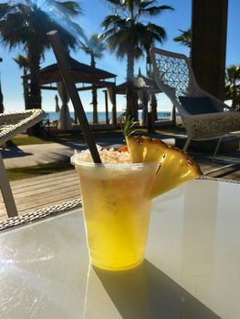 Delicious refreshing yellow cocktail with pineapple on the sea and palm trees background