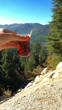 Tulip shaped cup of Turkish tea in girl's hand with mountains and blue sky view