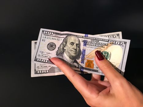 A Woman's Hand Holding two 100 Dollar Bills Banknotes on a grey background