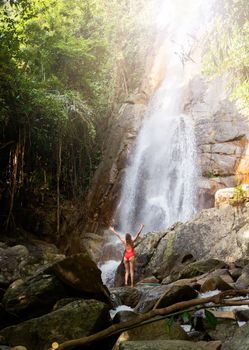 Beautiful young slim blonde woman with curly hair, wearing in red swimsuit is enjoy in lagoon of huge tropical waterfall in jungle. Travel concept. Sexy woman wearing red swimsuit in the jungle