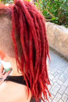 Red dreadlocks of on the back of a girl's head, with the rest of her hair almost shaved off, walking on a sidewalk.