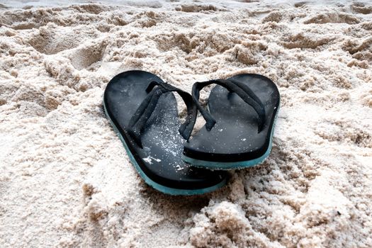A pair of flip flops, slightly overlapping in the sand on the beach, with a turquoise sole and slightly soiled with sand.