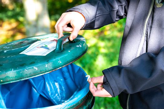 Brandenburg, Brandendburg/Germany - 05.09.2019: A person throws an extinguished cigarette butt into a bin with a hinged lid and a blue bin bag