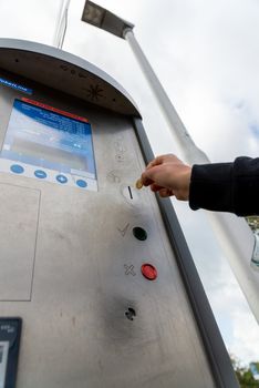 Fehmarn, Schleswig-Holstein/Germany - 05.09.2019: A hand wants to throw a coin into a parking ticket machine, which has a display, a confirmation button and a cancel button, photographed from below.