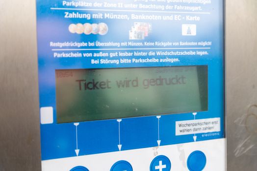 Fehmarn, Schleswig-Holstein/Germany - 05.09.2019: A display of a parking ticket machine showing that the ticket is being printed. On the display you can also see a part of the operation of the machine.