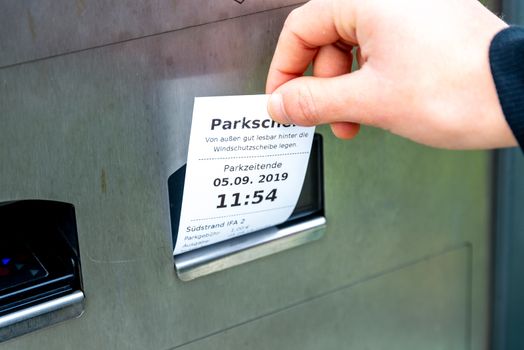Fehmarn, Schleswig-Holstein/Germany - 05.09.2019: A hand pulls a parking ticket out of a parking ticket machine, on which it is noted when the parking time ends and where you can park. The machine is made of metal.