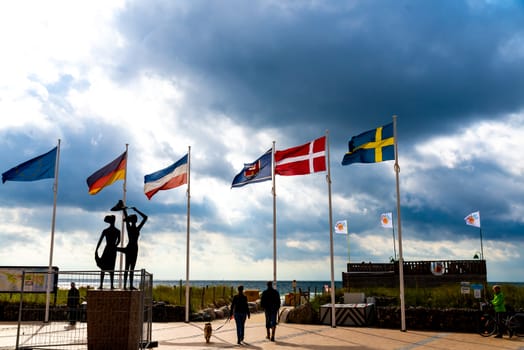 Fehmarn, Schleswig-Holstein/Germany - 05.09.2019: A view towards the southern beach of Fehmarn in Germany with pedestrians, national flags and the sculpture Girl from the southern beach in backlight.