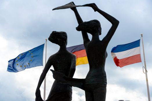 Fehmarn, Schleswig-Holstein/Germany - 05.09.2019: The sculpture Girl at the southern beach with flags of Germany, Netherlands and Europe in the background in backlight.
