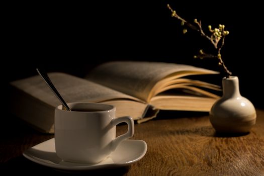 An open book and a cup of coffee on the table. Vase with a branch of apricots and a book on the table. Reading a book in a cafe. Stylish photo of the coffee house. A cup of coffee in the evening light.