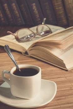 An open book and a cup of coffee on the table. Glasses. A cup of coffee in the evening light.