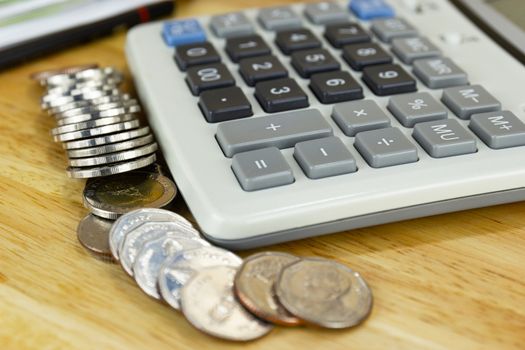 the stack of coin with calculator on wood table at office, concept of calculating expenses, incomes and expenses.