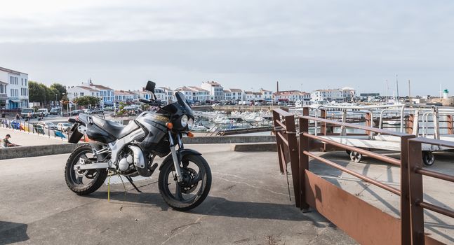 Yeu island, France - September 18, 2018: Motorcycle parked in harbor port Joinville near boats on a summer day