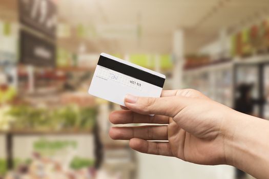 female hand holding credit card with blurry supermarket background