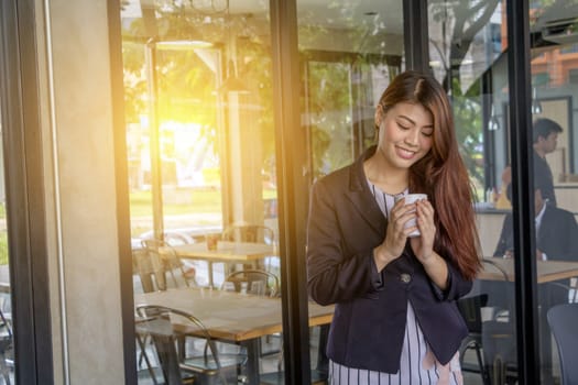 Asian business woman standing to drink coffee, In front of a coffee shop.