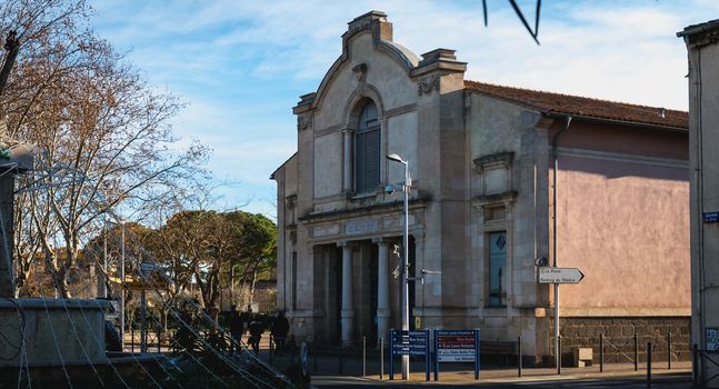 Marseillan, France - December 30, 2018: Man in wheelchair in front of the Henri Maurin theater in the historic city center on a winter day