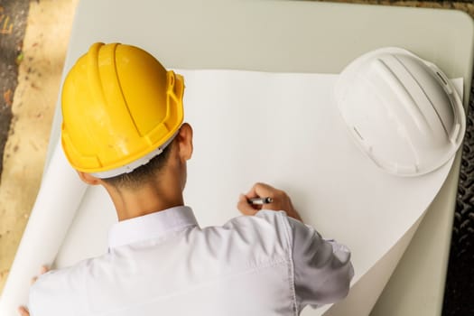 Young Asia man engineer wearing safety yellow helmet in white shirt checking construction site building.