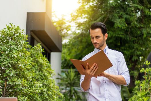 A young man reading a book in the garden. There's a notebook on the table to use information and work.Young man working in the garden.