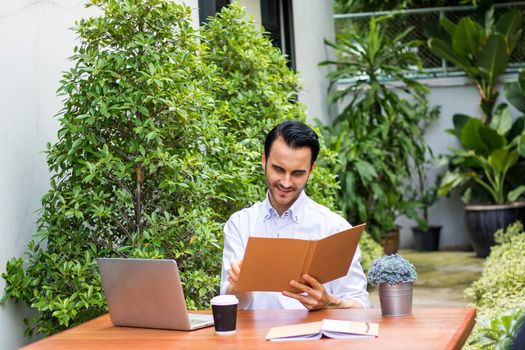 A young man reading a book in the garden. There's a notebook on the table to use information and work.Young man working in the garden.Young man working in the garden.