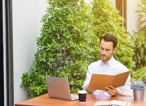 A young man reading a book in the garden. There's a notebook on the table to use information and work.Young man working in the garden.