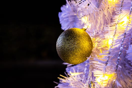 Closeup of white Christmas-tree with golden ball hanging decorations with golden lights glowing.