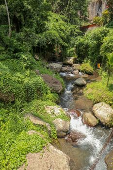 River bed in Pakerisan valley with wild water and big boulders. Water rolling over rocks in a river bed at a funeral complex in Tampaksiring. Gunung Kawi, Bali, Indonesia. Tropical vegetation.